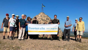 Eleven people standing at the top of a mountain holding a Tiverton u3a banner 