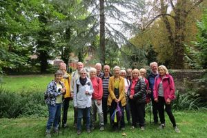 A large group of older adults are standing in a wooded parkland area, in front of a tree