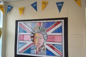 A piece of artwork, framed and on the wall, that shows a collage of the face of Queen Elizabeth II on a background of the union jack. Above the picture there is blue and yellow u3a bunting.