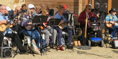 Four older adults sitting in front of microphones holding instruments.