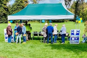 A green tent in a field with people milling in front of it, chatting.