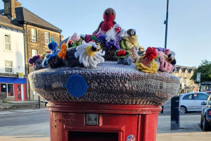 a postbox with a covering consisting of knitted flowers and a knitted robin