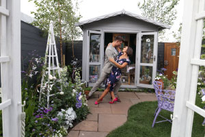 A man and woman dancing in a garden and looking into each others eyes.