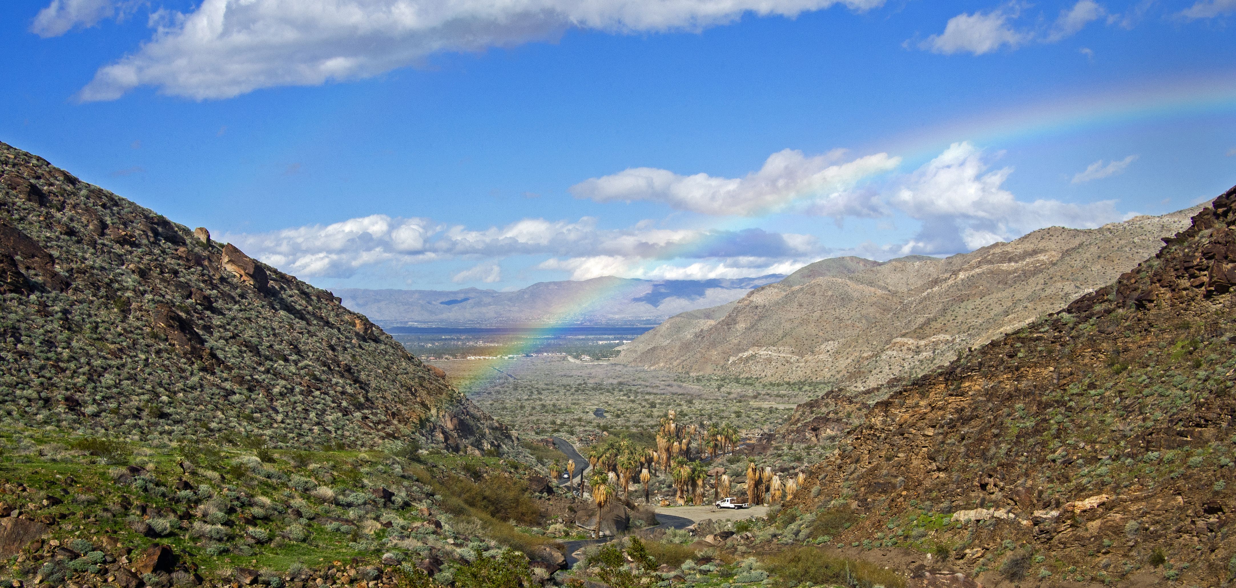 mountainous landscape with a rainbow across the mountains. Blue sky with white clouds behind 
