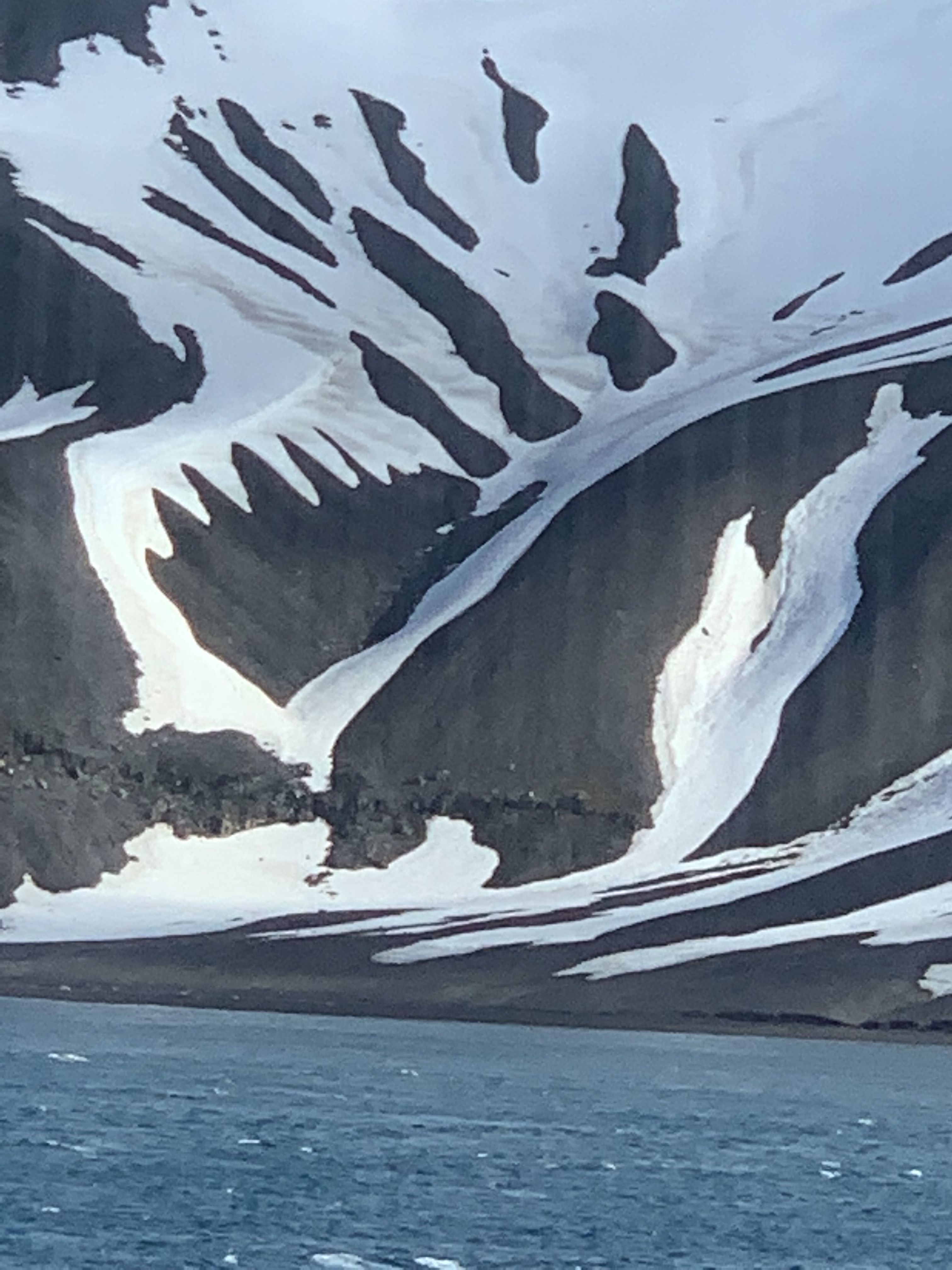 snow on rocky mountains, with water in the foreground