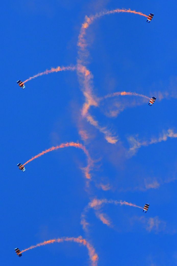 6 planes leaving orange cloud trails in a blue sky