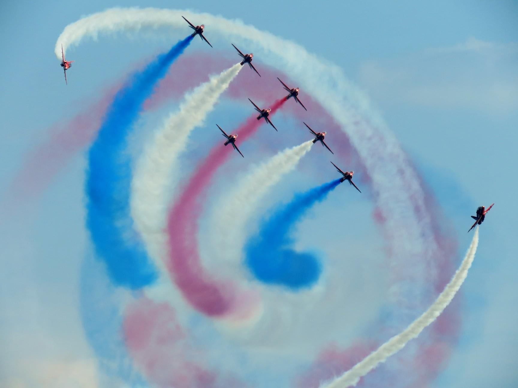 9 planes in formation in the sky, with red white and blue trails following them. 
