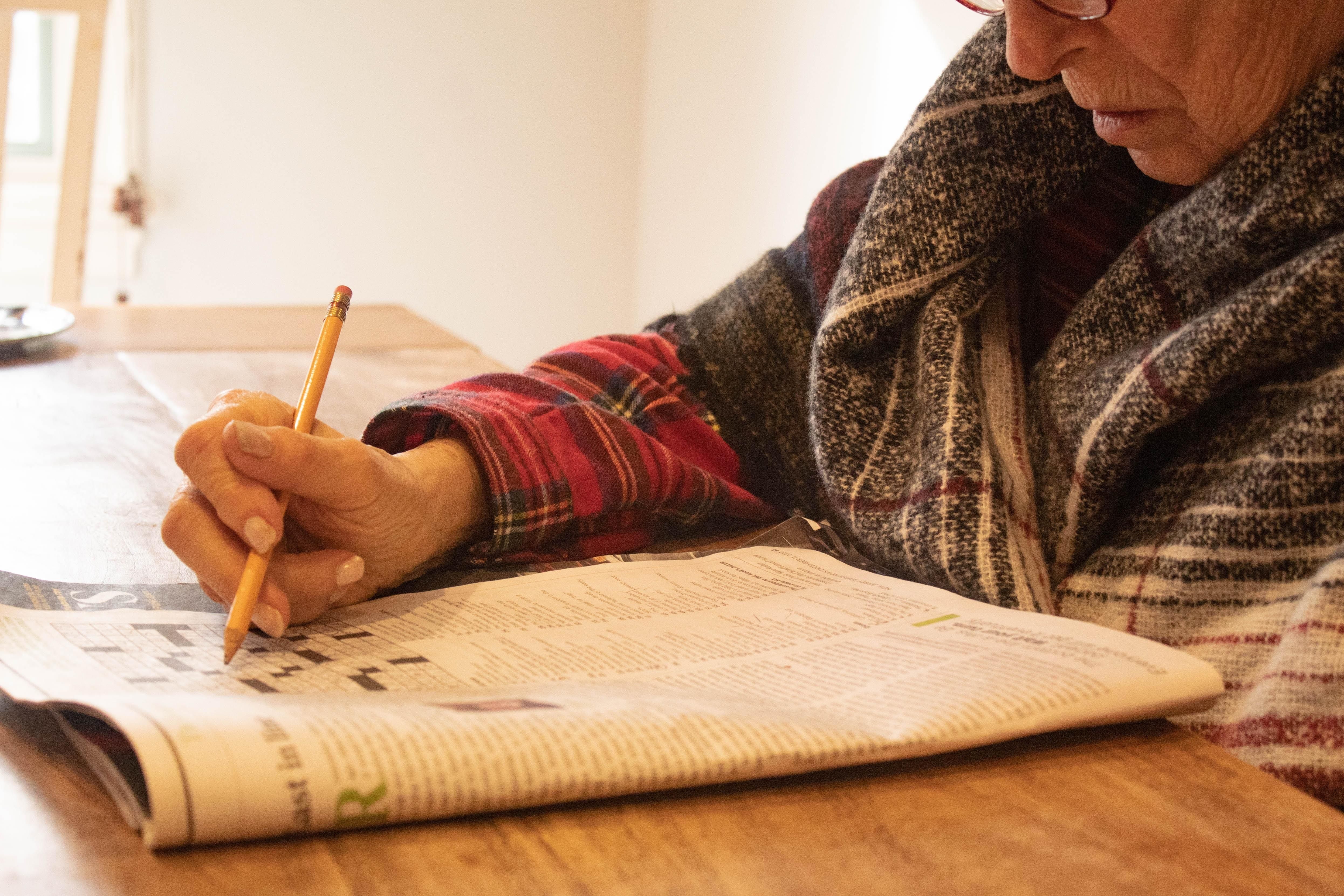 an older woman completing a crossword with pencil in hand