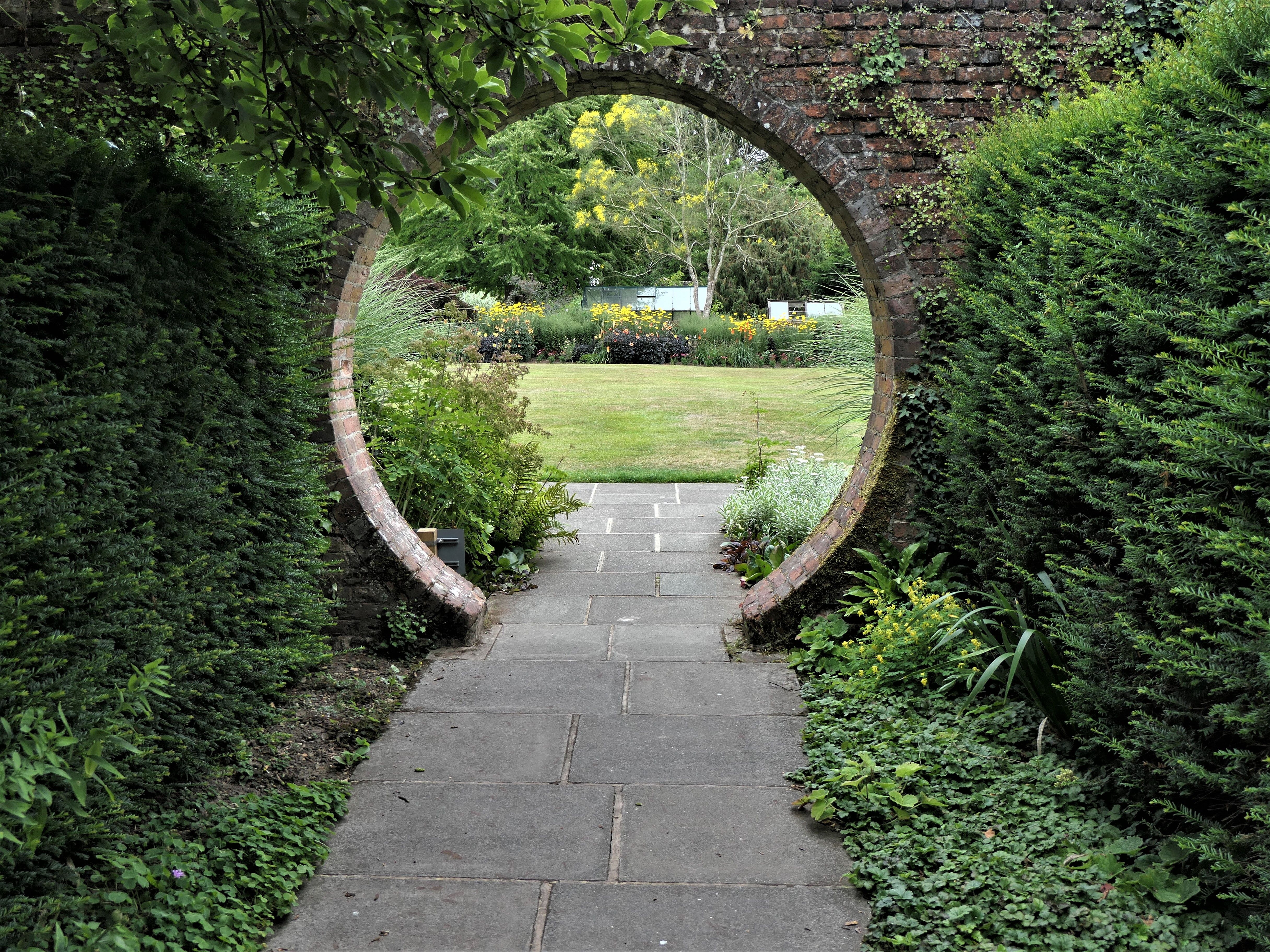 a path towards a garden, with a circular hole in a wall to walk through