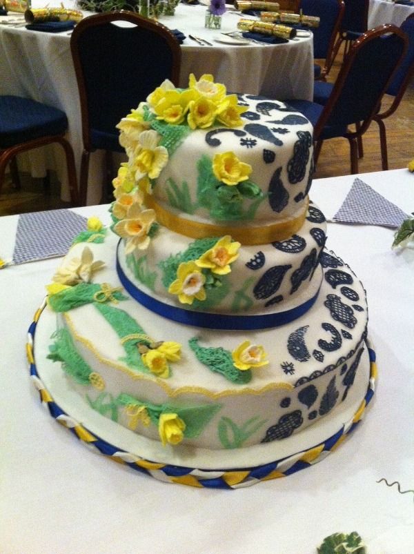a three tiered blue and yellow cake with daffodils as the primary decoration