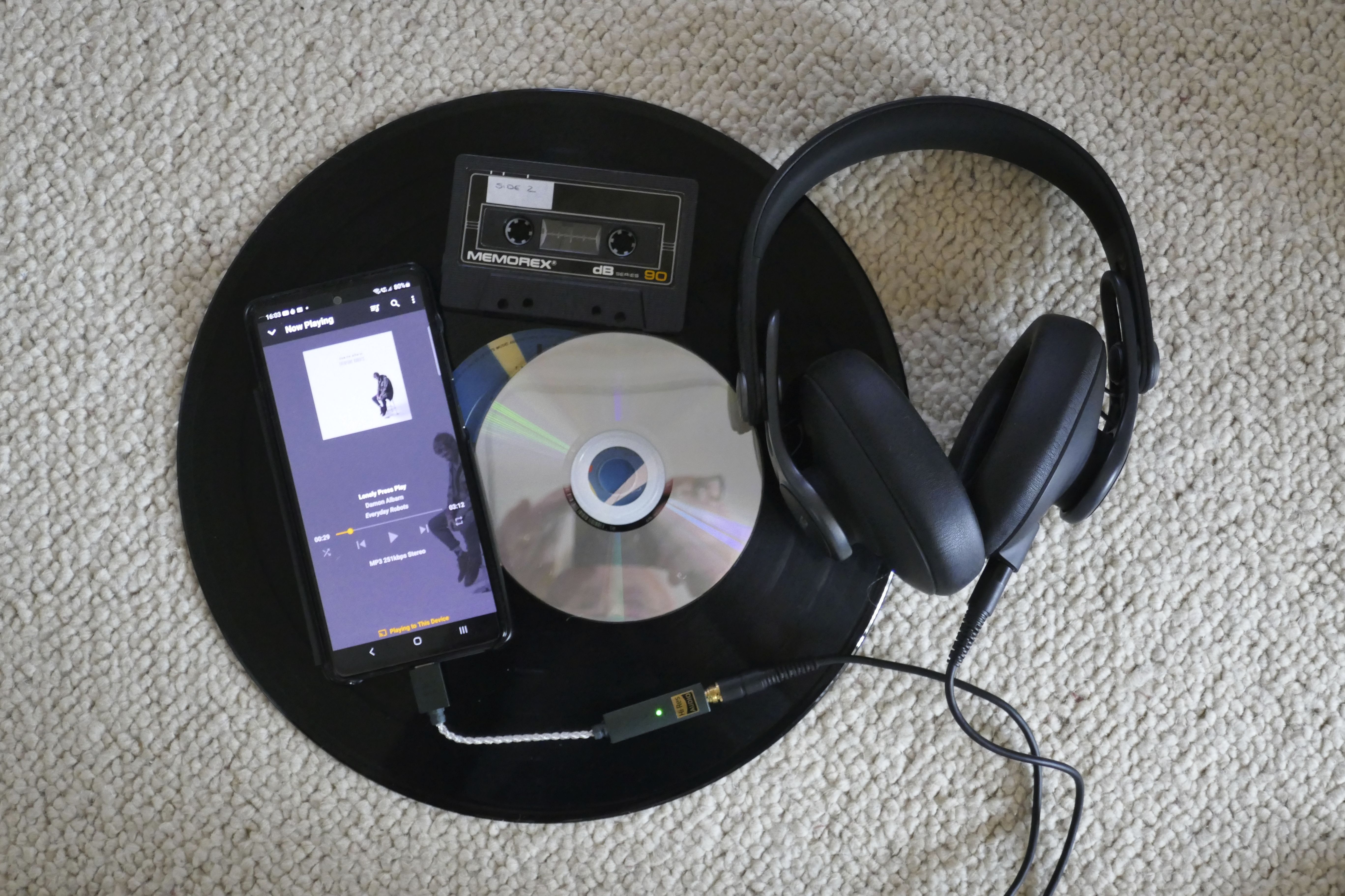 various ways to listen to music laid out on a carpet. Record, CD, overhead headphones, tape and smartphone