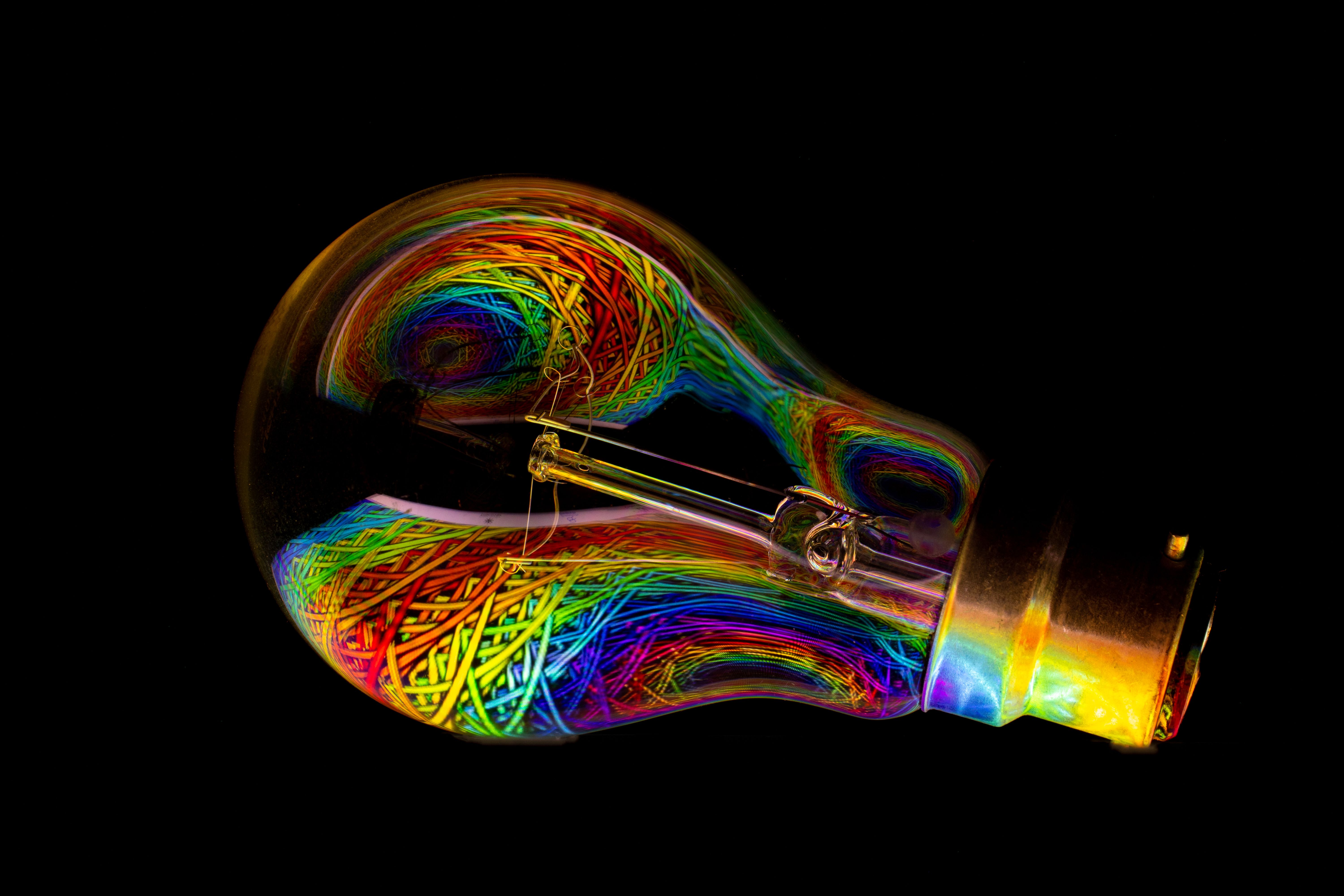 A lightbulb with bright multicoloured swirly patterns in it lies on a black background