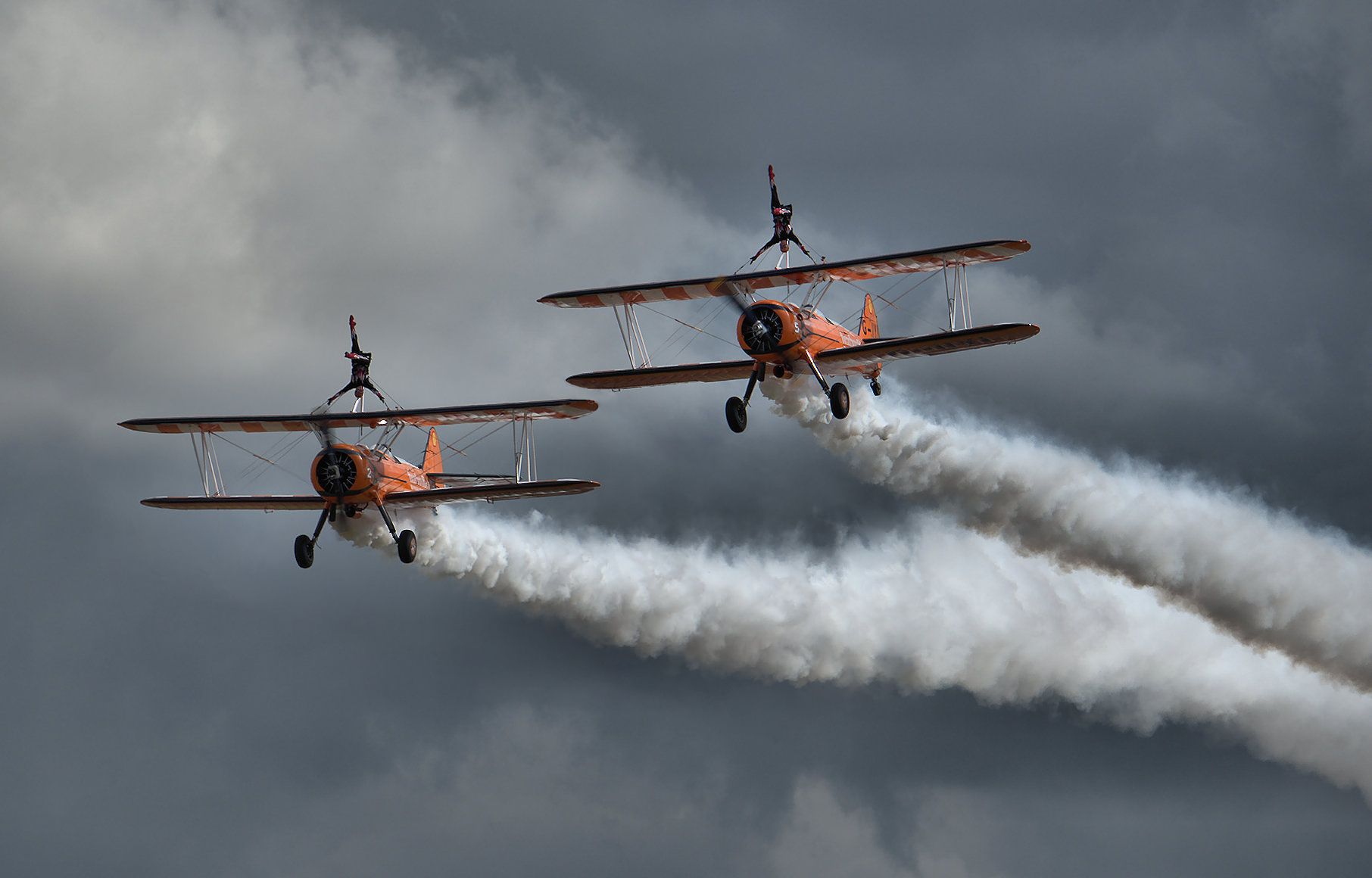 two people on top of planes with trail in sky