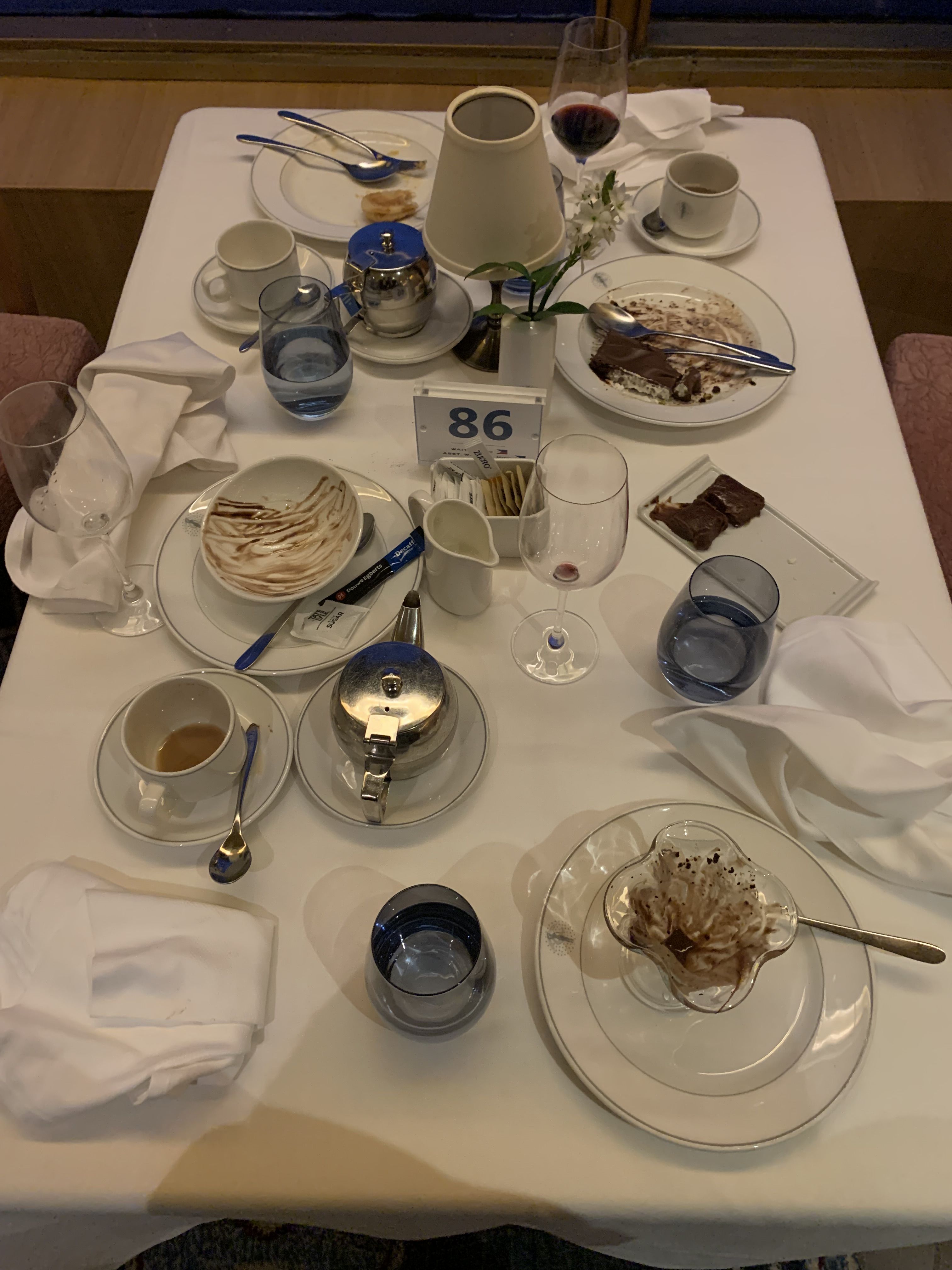 a table with a white tablecloth and empty bowls, plates, glasses and mugs