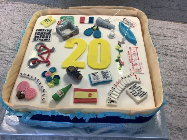 square cake with yellow number 20 in the middle and colourful u3a activities detailed on it in icing, all on a silver cake board