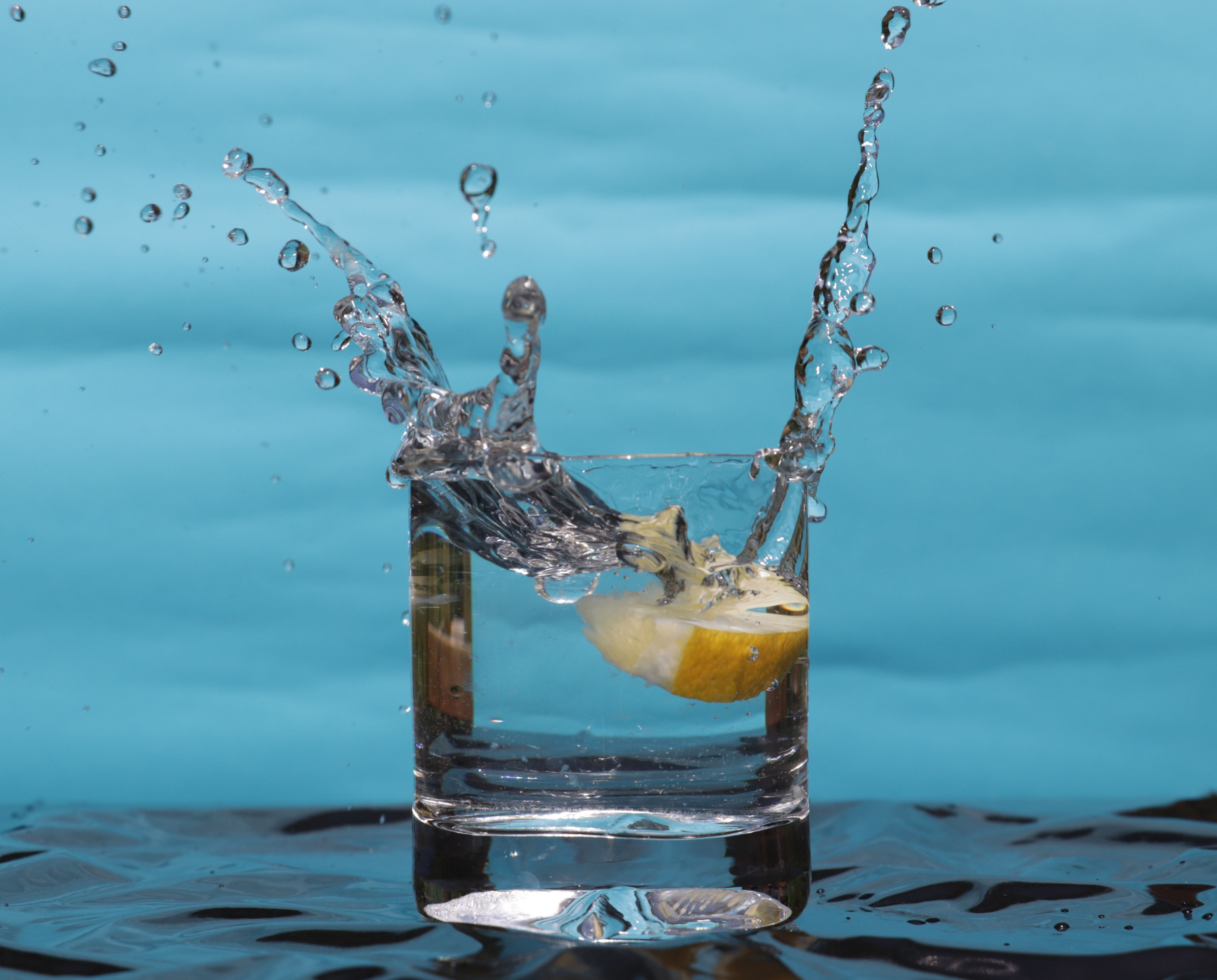 a clear photo of a glass with water splashing out of it, and a slice of lemon falling into it